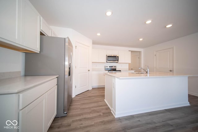 kitchen featuring a center island with sink, white cabinets, light hardwood / wood-style floors, and appliances with stainless steel finishes