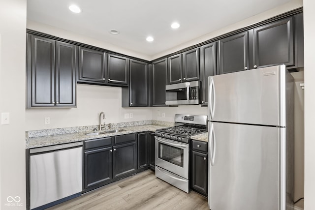 kitchen with light stone countertops, appliances with stainless steel finishes, light hardwood / wood-style flooring, and sink