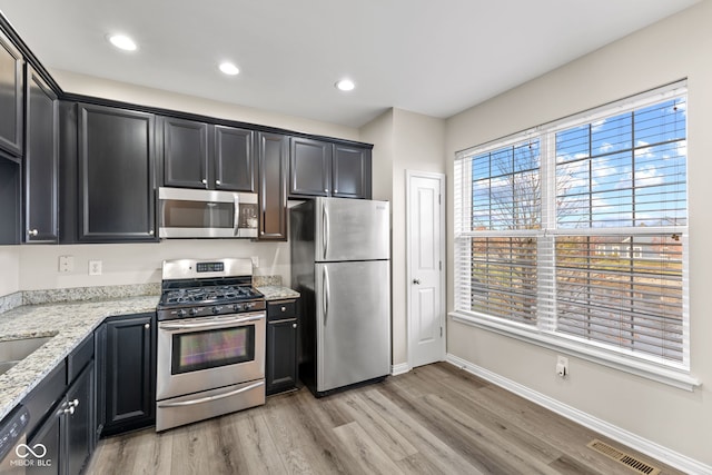 kitchen with light stone countertops, appliances with stainless steel finishes, and light hardwood / wood-style flooring