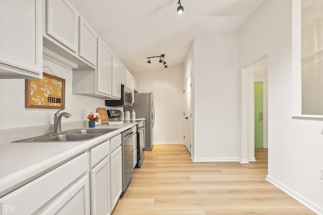 kitchen with appliances with stainless steel finishes, white cabinets, track lighting, and light wood-type flooring