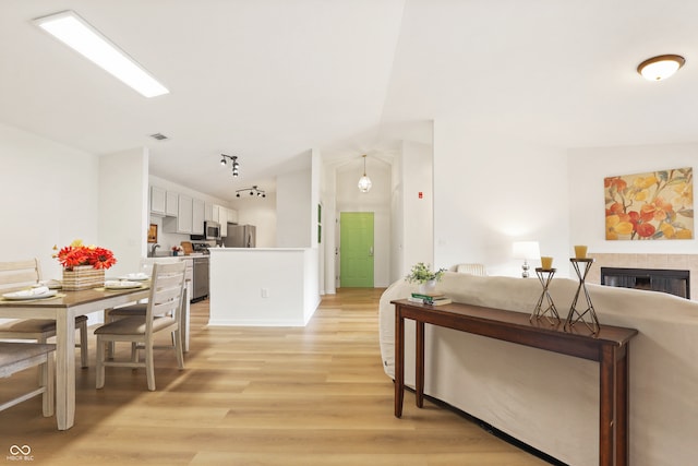 kitchen with stainless steel appliances, a tile fireplace, light hardwood / wood-style flooring, white cabinetry, and hanging light fixtures