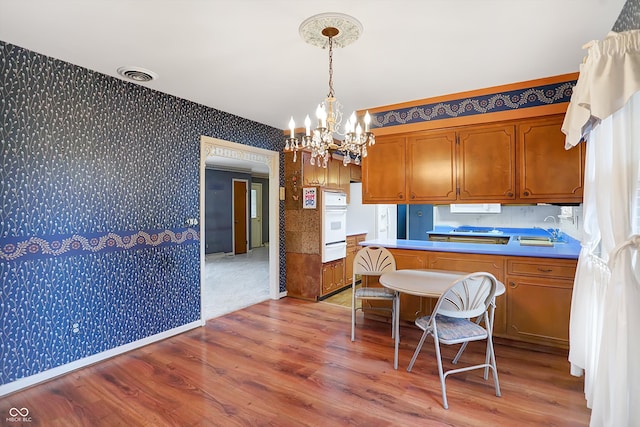 kitchen featuring hanging light fixtures, light wood-type flooring, an inviting chandelier, and white oven