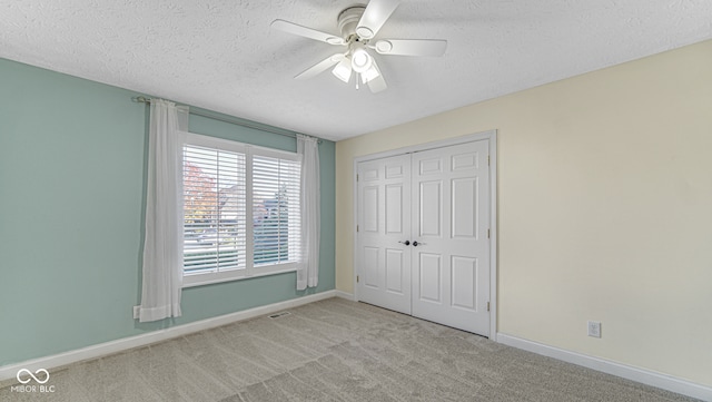 unfurnished bedroom featuring ceiling fan, a closet, light carpet, and a textured ceiling