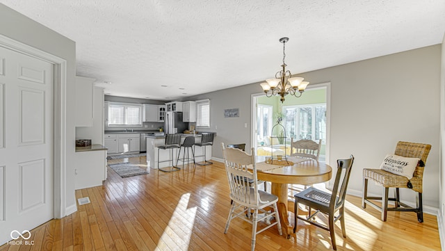 dining space featuring visible vents, baseboards, a textured ceiling, light wood-style floors, and a chandelier