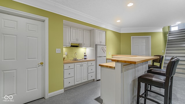 kitchen with a breakfast bar area, wooden counters, freestanding refrigerator, white cabinets, and a sink