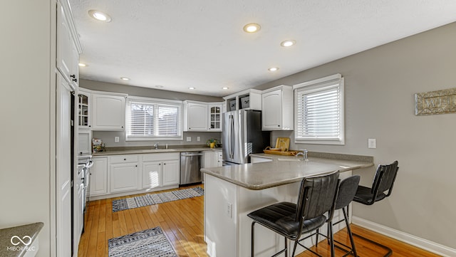 kitchen featuring white cabinets, stainless steel appliances, kitchen peninsula, and light hardwood / wood-style floors