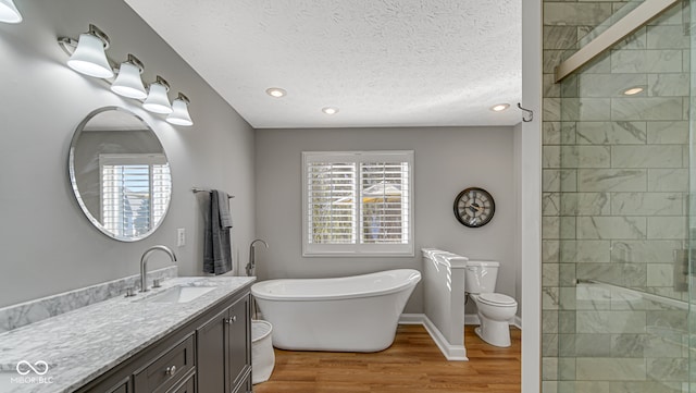 full bath with a stall shower, a soaking tub, wood finished floors, a textured ceiling, and vanity