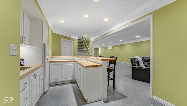 kitchen with kitchen peninsula, ornamental molding, white cabinets, white fridge, and butcher block counters