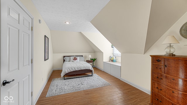 bedroom with lofted ceiling, a textured ceiling, and light hardwood / wood-style flooring