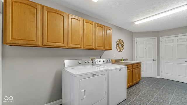 laundry area with a textured ceiling, washer and clothes dryer, cabinet space, and baseboards