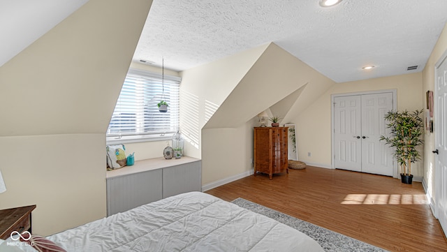 bedroom with light wood finished floors, lofted ceiling, visible vents, a textured ceiling, and baseboards