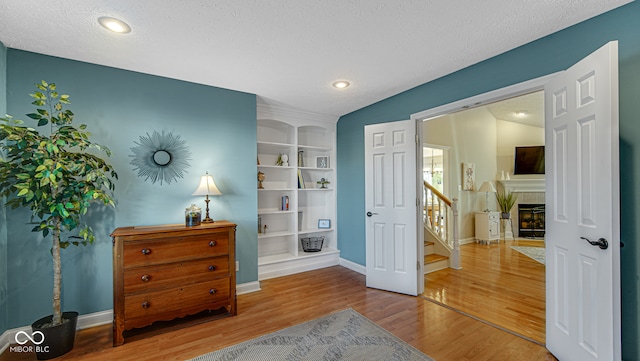 interior space featuring vaulted ceiling, built in features, a fireplace, a textured ceiling, and wood-type flooring