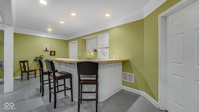 kitchen featuring a kitchen bar, kitchen peninsula, white cabinetry, and crown molding