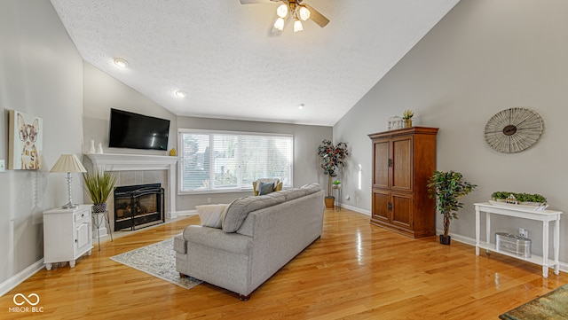 living room featuring high vaulted ceiling, ceiling fan, a textured ceiling, a fireplace, and light hardwood / wood-style floors