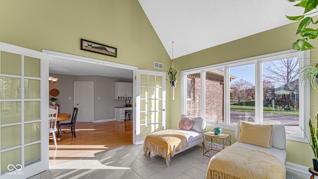 living area featuring light tile patterned floors, high vaulted ceiling, visible vents, baseboards, and french doors