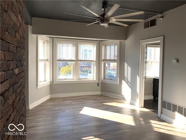 unfurnished room with hardwood / wood-style floors, ceiling fan, and brick wall