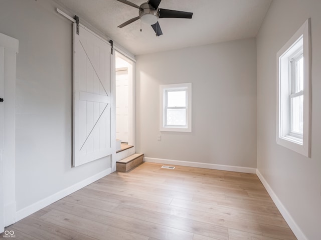 empty room with a barn door, ceiling fan, light hardwood / wood-style floors, and a textured ceiling