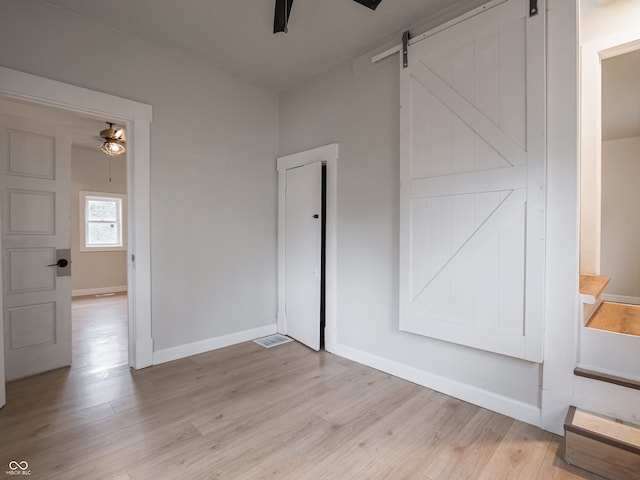 empty room featuring ceiling fan, a barn door, and light wood-type flooring