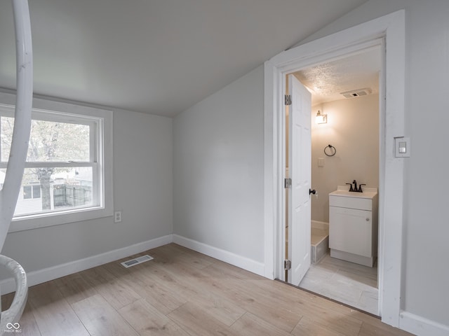 additional living space featuring light wood-type flooring, sink, and vaulted ceiling