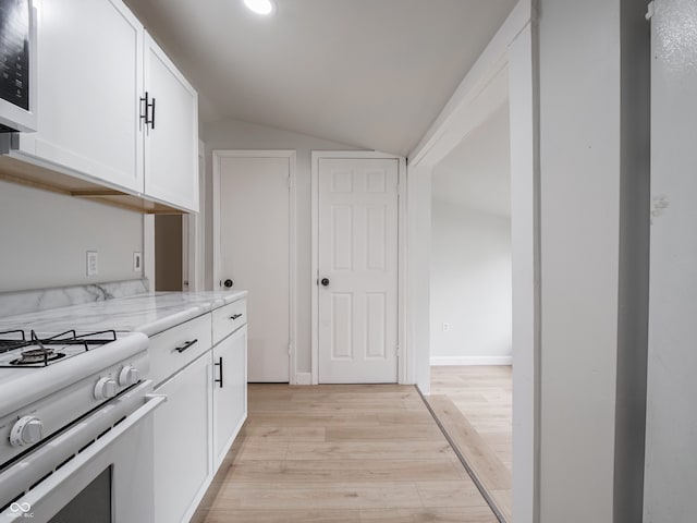 kitchen featuring white cabinets, white range, vaulted ceiling, light wood-type flooring, and light stone counters