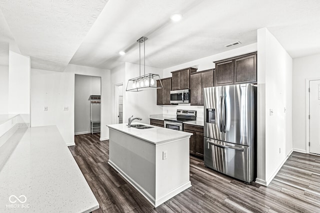 kitchen with sink, dark wood-type flooring, hanging light fixtures, stainless steel appliances, and a kitchen island with sink