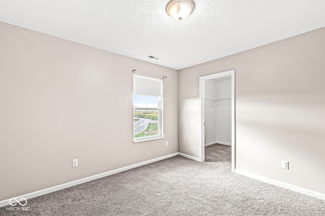 unfurnished bedroom with a walk in closet, a closet, carpet floors, and a textured ceiling