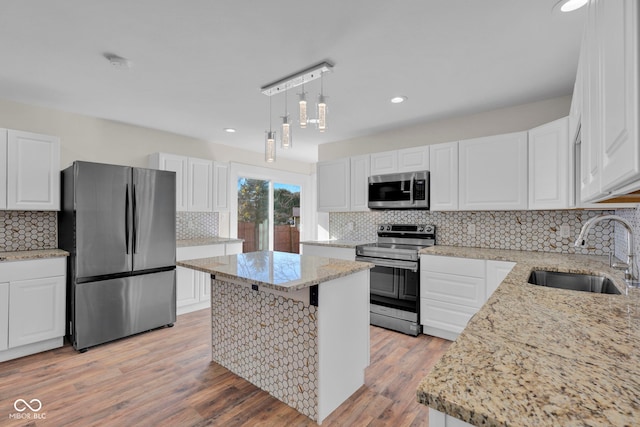 kitchen with appliances with stainless steel finishes, sink, white cabinetry, light hardwood / wood-style floors, and a kitchen island