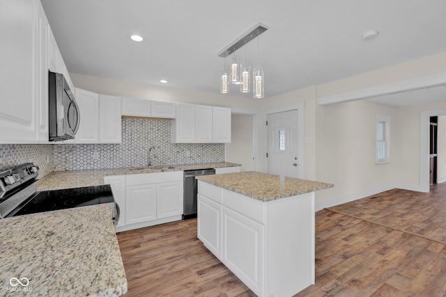 kitchen with light hardwood / wood-style flooring, appliances with stainless steel finishes, decorative light fixtures, a kitchen island, and white cabinetry