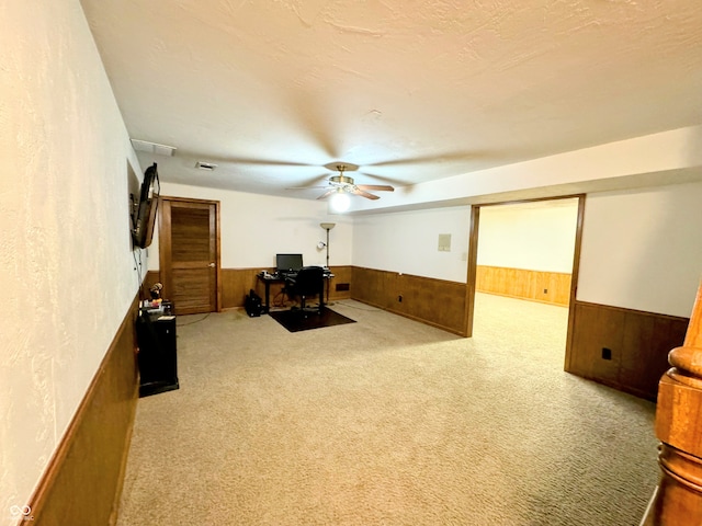 interior space featuring ceiling fan, wood walls, light colored carpet, and a textured ceiling