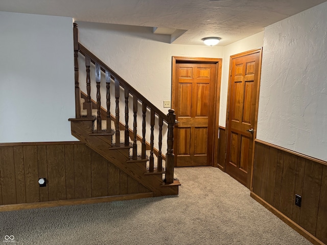 foyer featuring carpet flooring, wood walls, and a textured ceiling