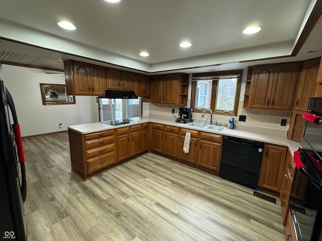 kitchen featuring decorative backsplash, kitchen peninsula, light wood-type flooring, sink, and black appliances