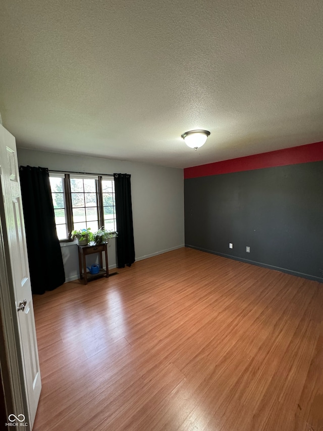 empty room with light wood-type flooring and a textured ceiling