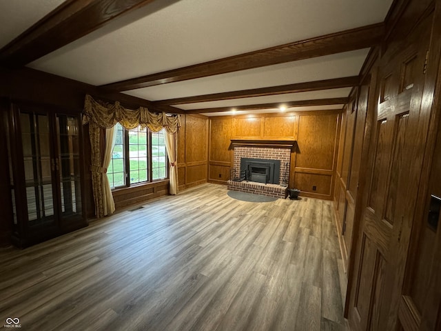 unfurnished living room with beam ceiling, wood walls, hardwood / wood-style floors, and a brick fireplace