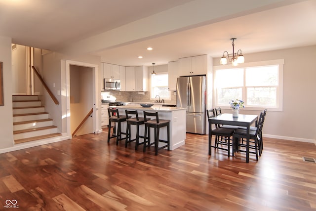 kitchen with appliances with stainless steel finishes, white cabinets, a center island, dark hardwood / wood-style floors, and hanging light fixtures