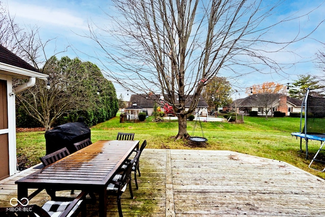 wooden deck with a yard, outdoor dining space, and a trampoline