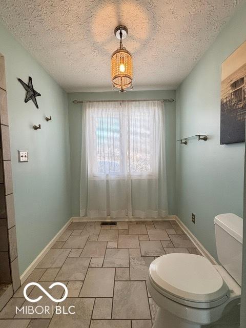 bathroom with visible vents, toilet, a textured ceiling, and baseboards