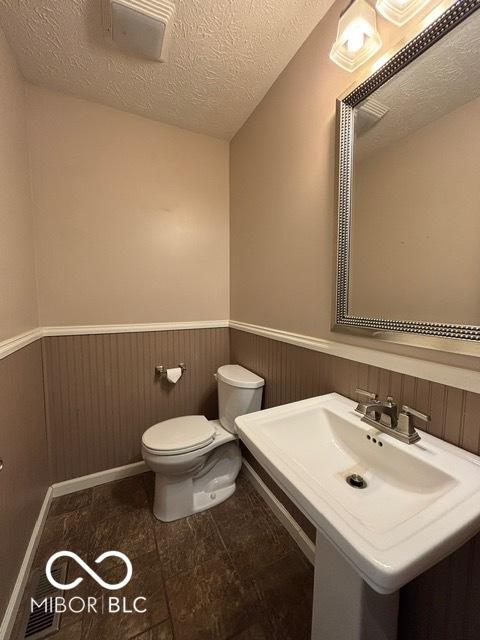 bathroom featuring toilet, a wainscoted wall, a sink, and a textured ceiling