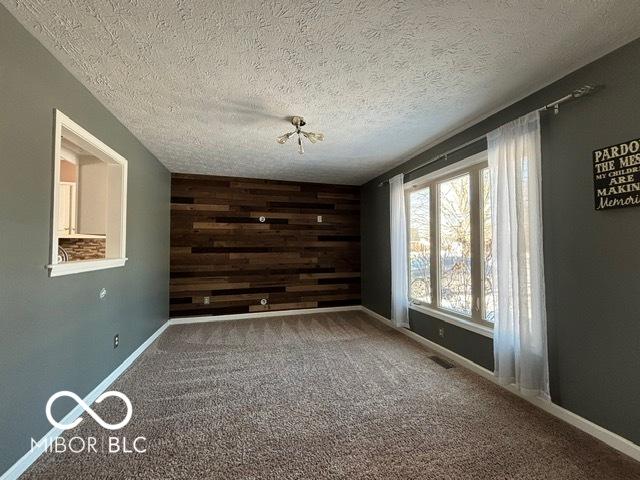 carpeted empty room with visible vents, an accent wall, wooden walls, a textured ceiling, and baseboards