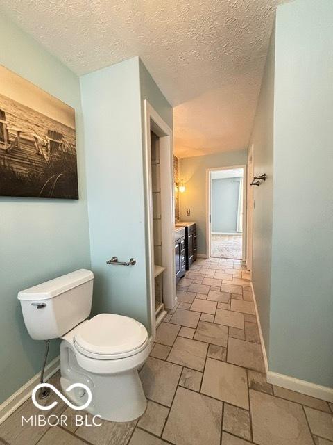 bathroom featuring toilet, stone finish floor, baseboards, and vanity