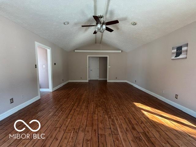 unfurnished living room featuring dark wood-type flooring, lofted ceiling, baseboards, and a ceiling fan