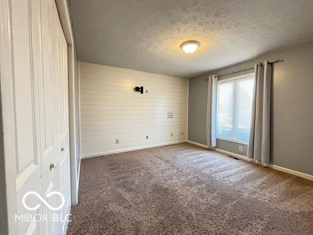 carpeted empty room featuring a textured ceiling, wood walls, visible vents, and baseboards