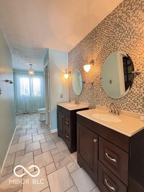 bathroom featuring baseboards, a sink, a textured ceiling, and toilet