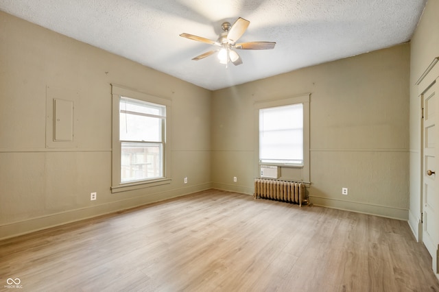 spare room with radiator, ceiling fan, electric panel, a textured ceiling, and light wood-type flooring