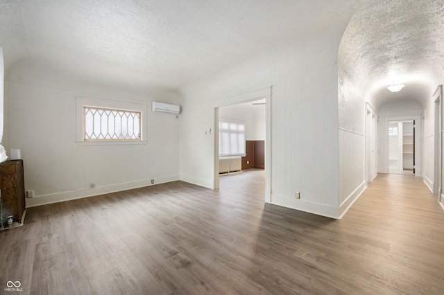 empty room featuring an AC wall unit, a wealth of natural light, hardwood / wood-style floors, and a textured ceiling