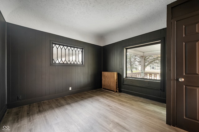 unfurnished room featuring a textured ceiling, light wood-type flooring, radiator, and wooden walls