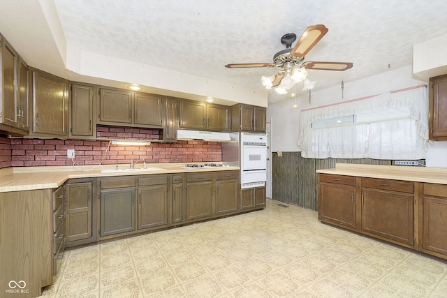 kitchen featuring tasteful backsplash, white gas stovetop, a textured ceiling, ceiling fan, and sink