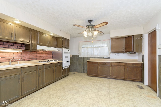 kitchen with ceiling fan, sink, stainless steel gas cooktop, backsplash, and a textured ceiling