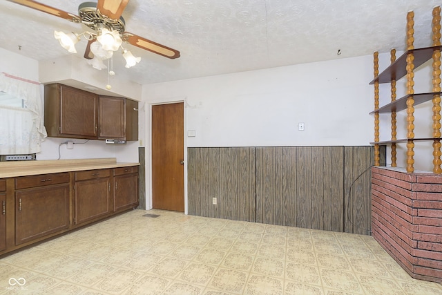 kitchen featuring wood walls, dark brown cabinets, ceiling fan, and a textured ceiling