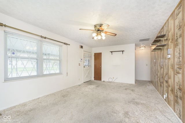 carpeted empty room featuring wooden walls, ceiling fan, and a textured ceiling