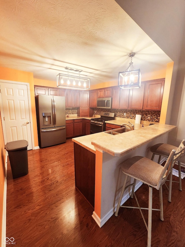 kitchen with pendant lighting, sink, a breakfast bar, stainless steel appliances, and kitchen peninsula